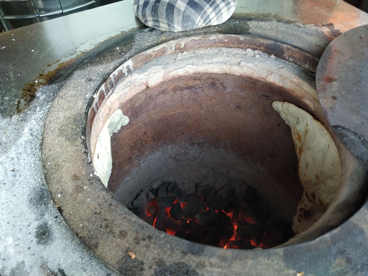 Fresh naan bread baking inside a traditional clay tandoor oven